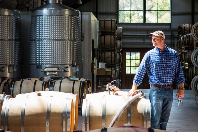 Winemaker in a winery inspecting wine barrels and tanks for quality control.